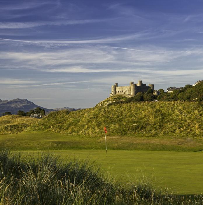 Ansicht eines Golfplatzes mit Flaggenstock, und Harlech Castle auf einem Hügel im Hintergrund