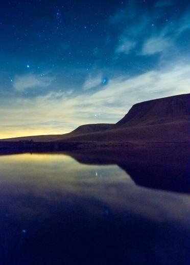 Mountain silhouetted against a starry sky captured in the Brecon Beacons.