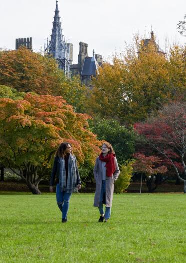 Two women walking in Bute Park with trees and Cardiff Castle in the background.