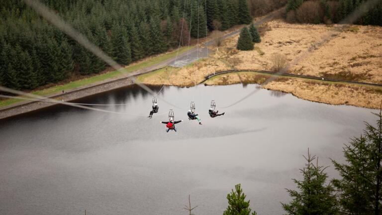 Four people travelling down a zip line above a lake.