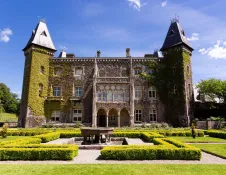 A grand house, covered in ivy with hedged gardens and fountain in the foreground.