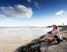 Woman with two small dogs sat on rocks on beach.