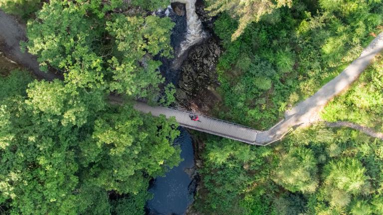 Luftaufnahme eines Mountainbikers, der über eine kleine, von Bäumen umgebene Brücke radelt