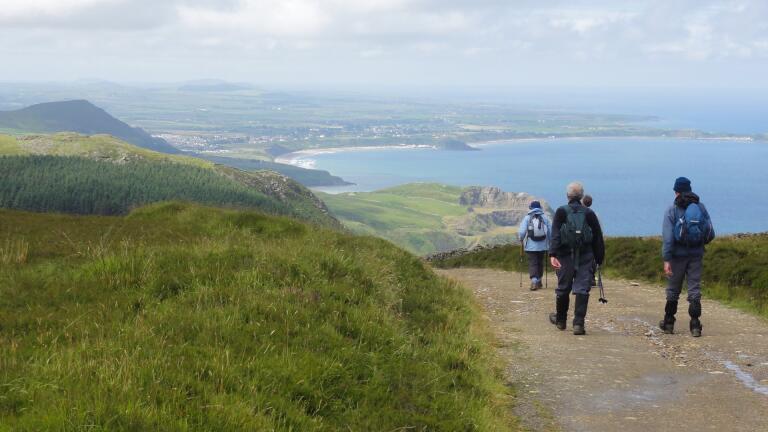 Three walkers on a coast path with views across a bay.