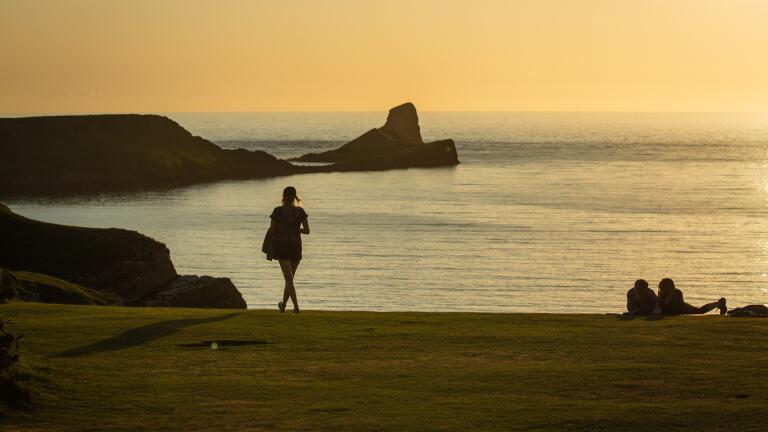 Sunset over a beach with people and features silhouetted over the sea.