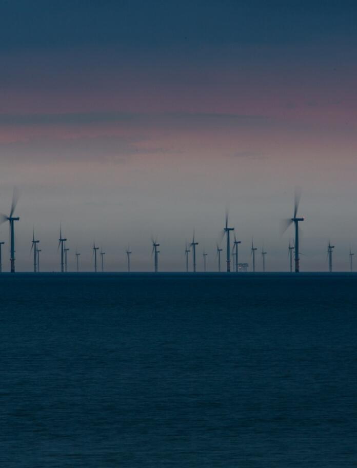 Views of wind turbines in the sea with sunset skies behind 