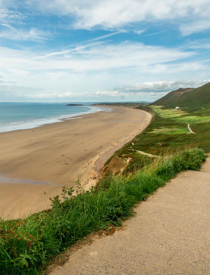 Woman with baby walking down pathway leading to beach.