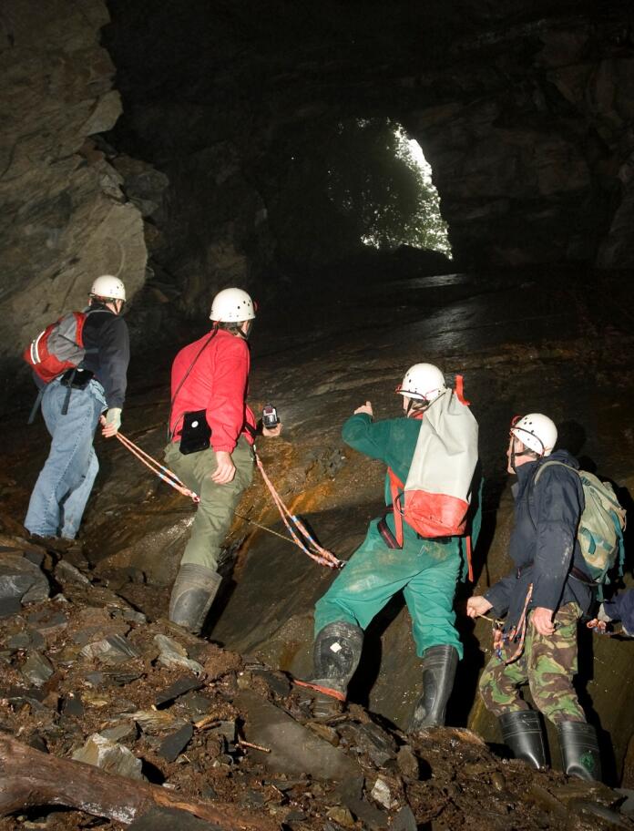 people with hard hats with lights on exploring mine with shaft of light coming through and rope being held
