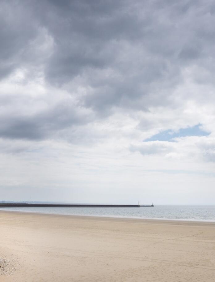 Ein flacher Sandstrand neben einer Promenade.