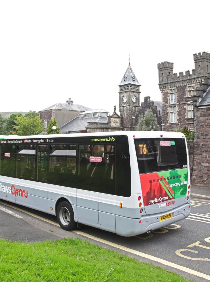 bus with the words TrawsCymru on it outside a stone building.