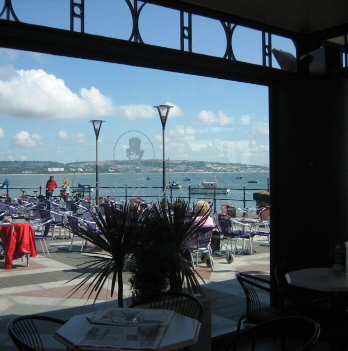 outside seating area with sea in background, viewed through cafe window.