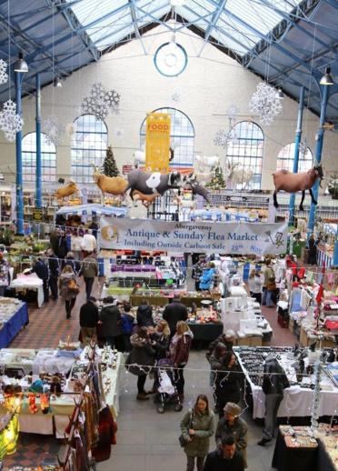 View of indoor market stalls and shoppers from above with models of farm animals hanging down.