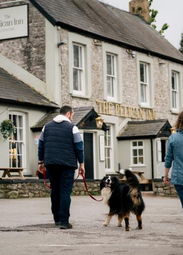 A family strolls towards the pub, their dog leading the way with a wagging tail, ready for a fun outing.