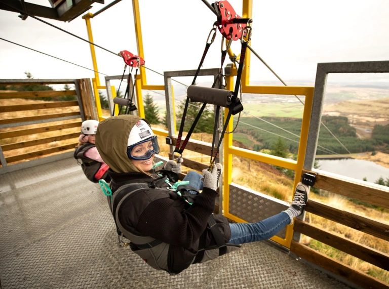 Zwei Personen an der Spitze einer sitzenden Seilbahn, bereit zum Start.