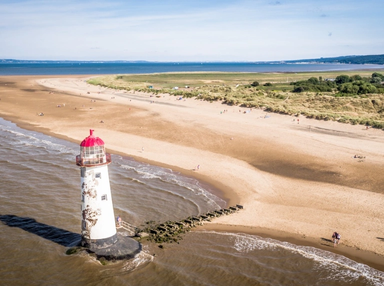 Ein Leuchtturm vor einem goldenen Sandstrand und grüner Dünenlandschaft
