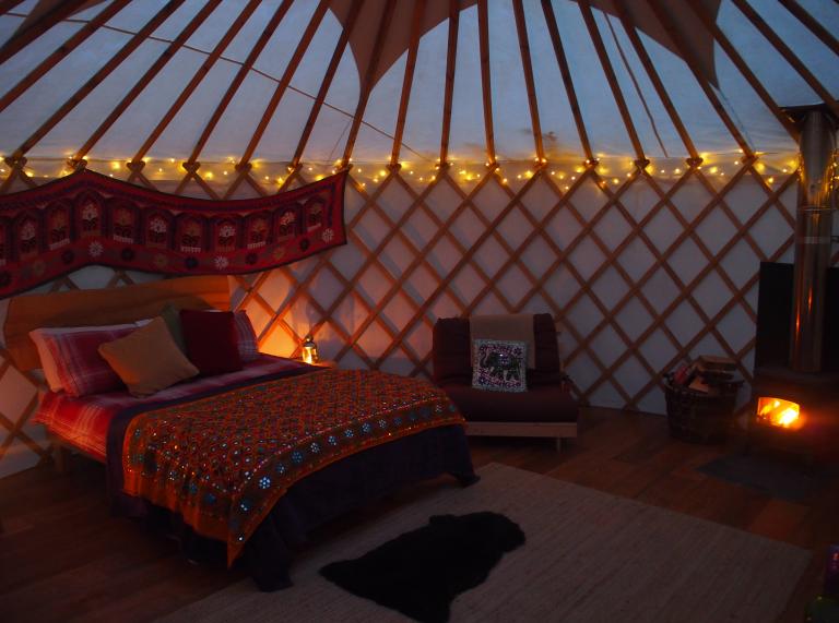 A double bed in a yurt with strung lights and wall hangings.