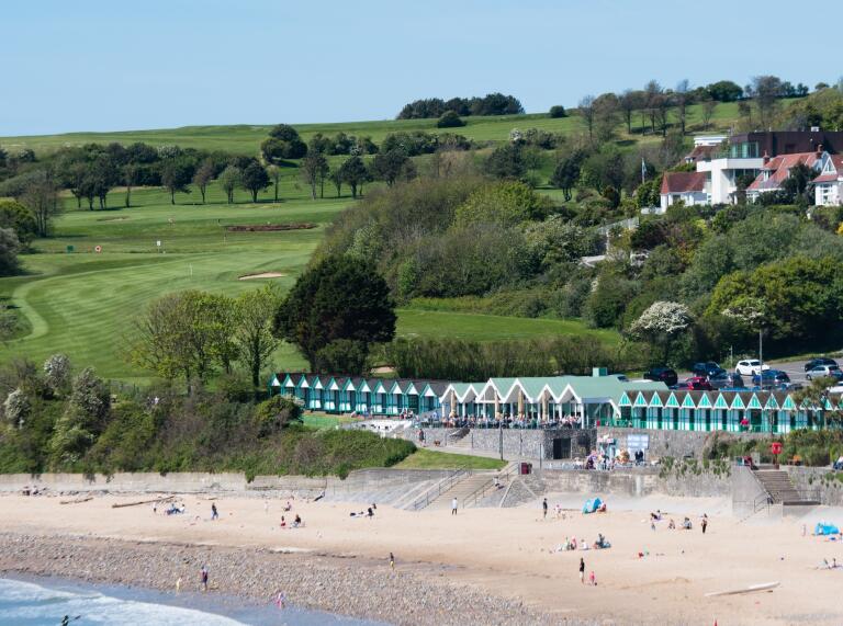 View from sea towards sandy beach with green beach huts.