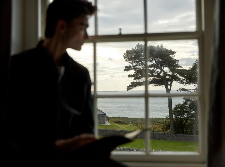 The shadow of a man reading a book and looking out of a window at the sea.