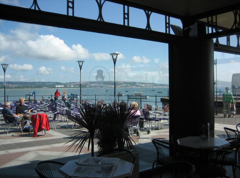 outside seating area with sea in background, viewed through cafe window.