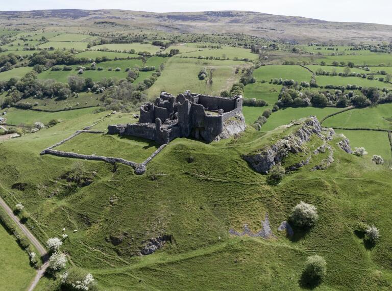 A ruined castle in green countryside from above.