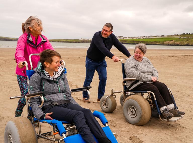 two people in beach wheelchairs and people pushing them.