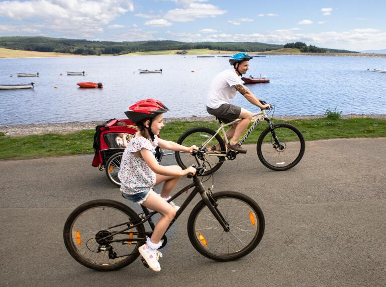 An adult and child using a flat cycle path by a wide lake.