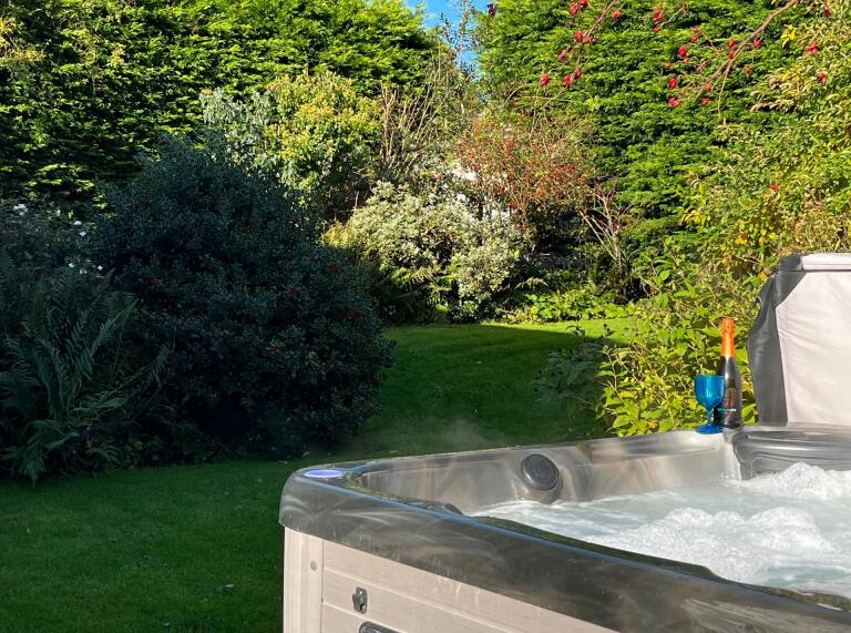 A bubbling hot tub in an enclosed garden, with a bottle of wine and a glass on the side.