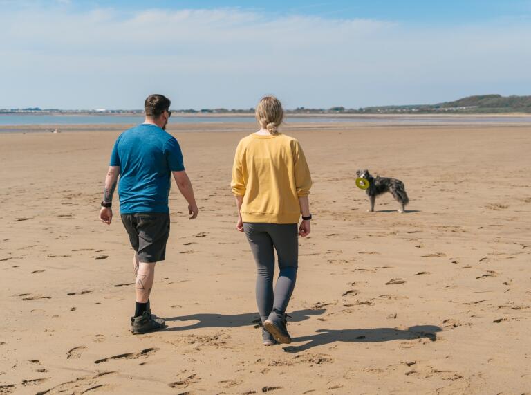 Two adults and a dog on a wide sandy beach.