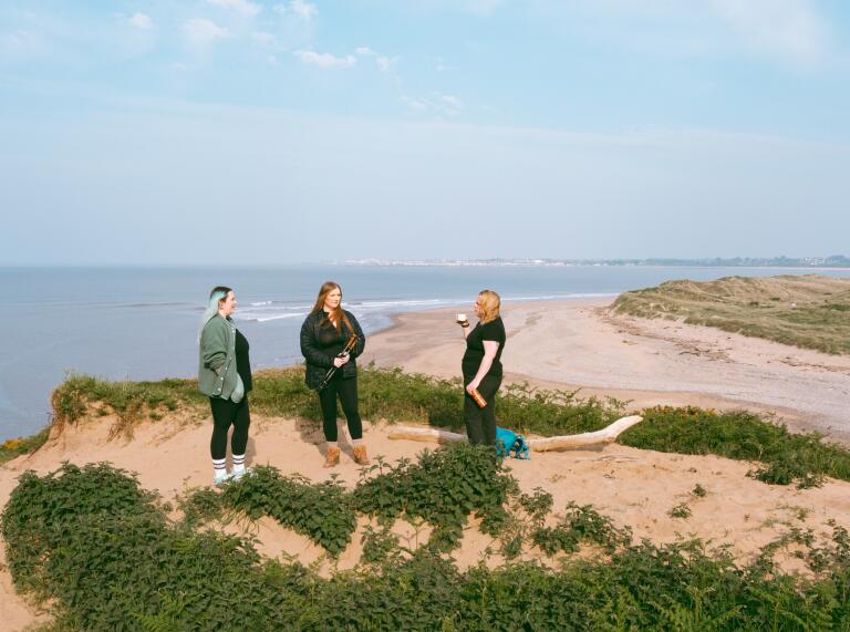 Three women on a cliff over looking a sandy beach.