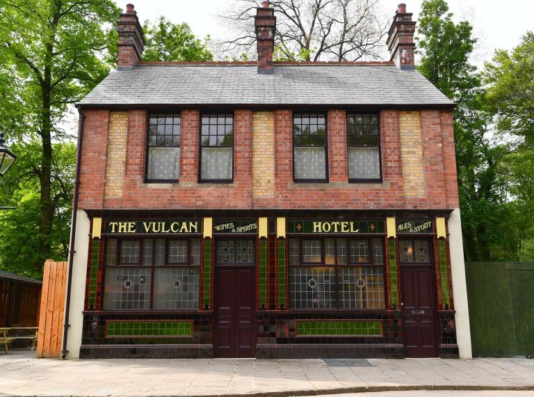 Exterior of an old pub with red brick walls, leaded windows and green tiles. 