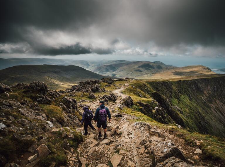 Two people walking along a mountain ridge.