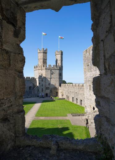 View through a castle window of the twin towers of a castle with welsh flags flying from them.