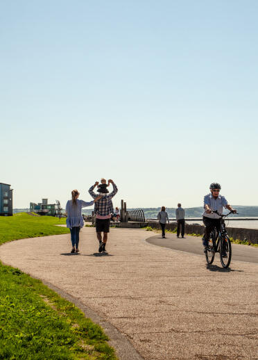 Spaziergänger und Radfahrer auf einem breiten Weg am Meer.