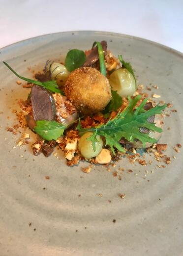 A breaded ball surrounded by duck meat and vegetables.