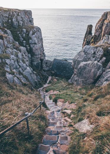 Steep stone steps down a coastal cliffside to a small stone chapel.