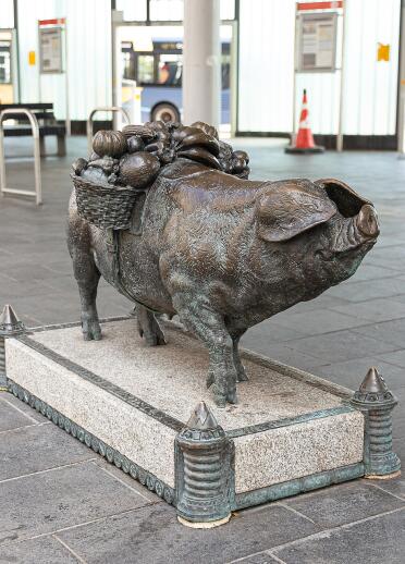 A bronze statue of a pig with a fruit basket on its back.
