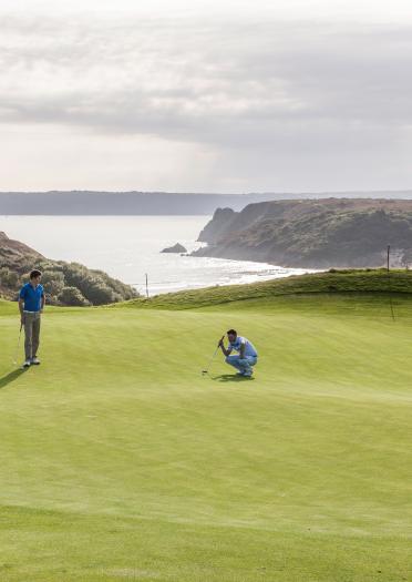 Two golfers on the green at Pennard golf club with the mountains and sea in background