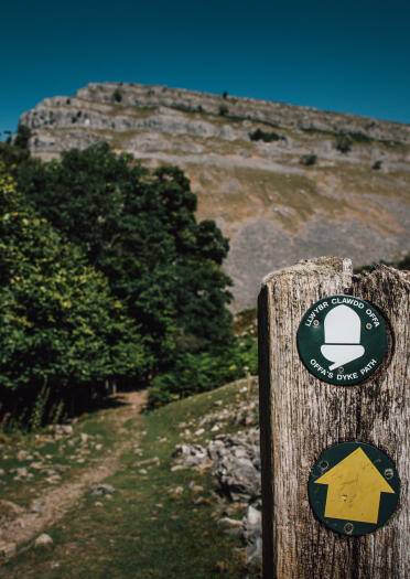 Ein Wanderzeichen an einem Pfosten mit einem Berg im Hintergrund.