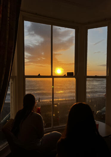 Two people watching a glorious sunset over the sea from a hotel bay window.
