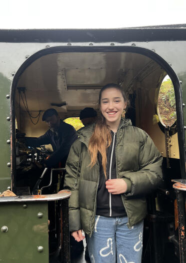A young lady standing on the footplate of a narrow gauge steam engine.