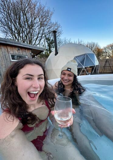 two women, one with a drink, in a hot tub.