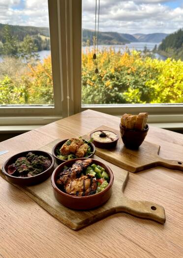 A tapas meal on wooden tables. A view of a lake can be seen through the window.