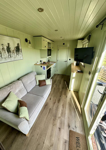 Inside a horse lorry that's been converted to accommodation - with a sofa, kitchen area and double doors.