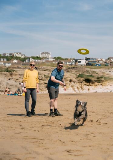 Two humans playing frizbee with a dog on a beach.