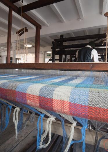blanket on weaving machine, with man weaving in background.