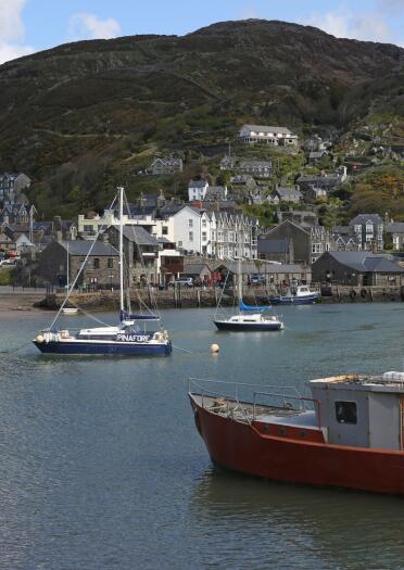 small boats in Barmouth harbour and houses and hills in the background.