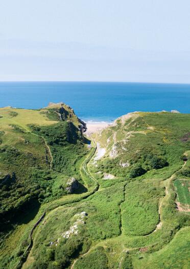 Aerial view of a valley, with a footpath leading to a small cove by the sea.