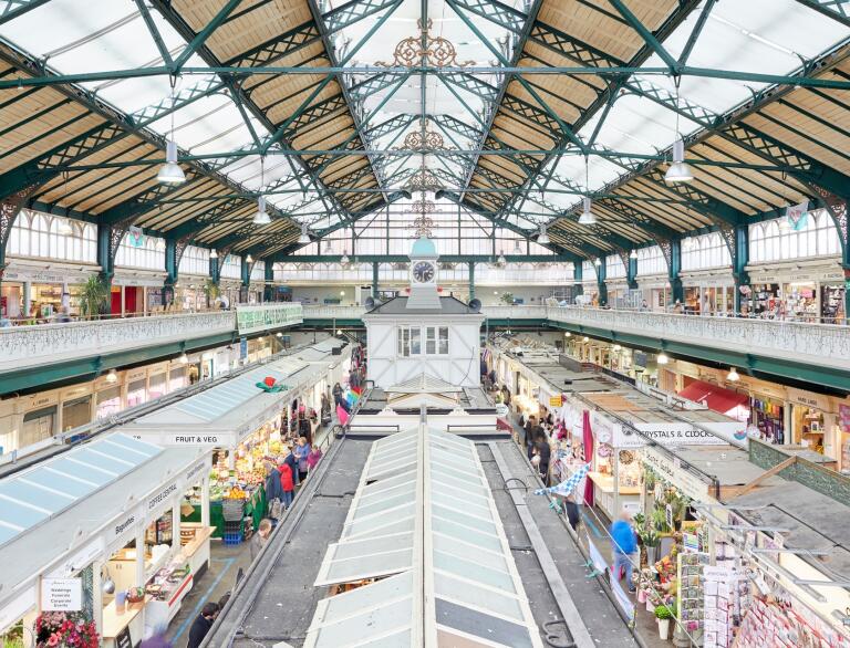 An indoor market under a triangular roof with skylights. There are lots of different stalls in rows.