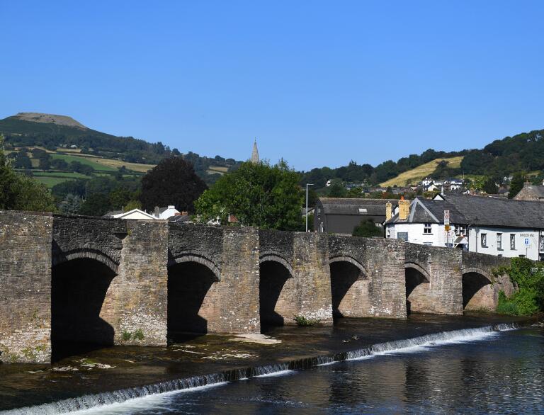 stone bridge on river, with town and hills in background. 