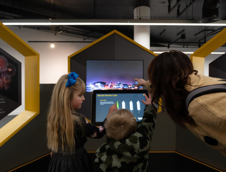 Two children and an adult interacting with a display screen.